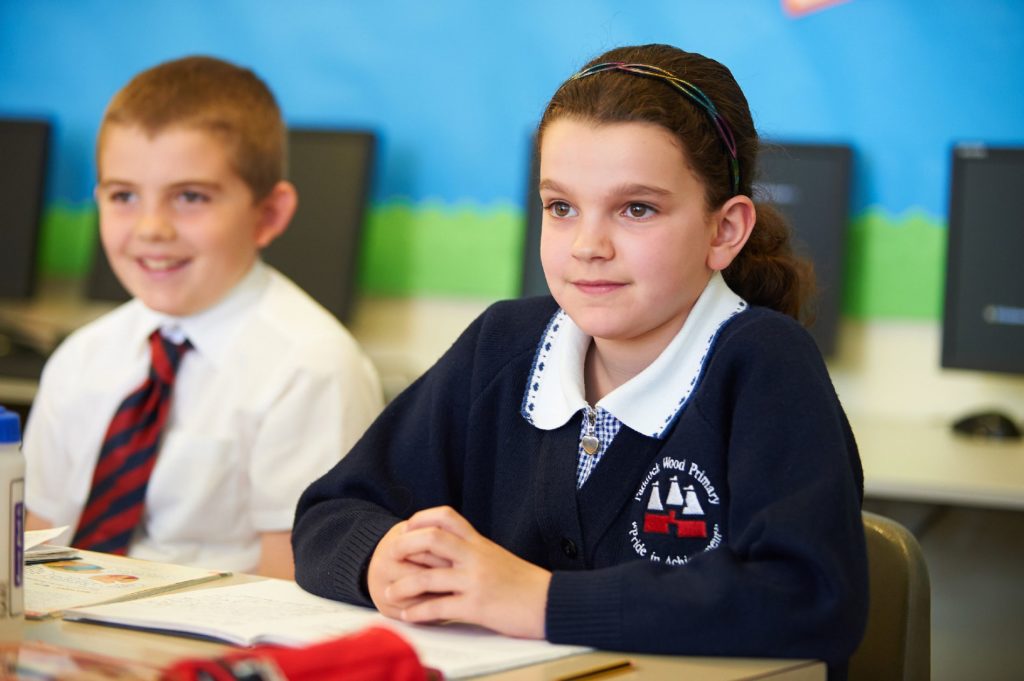 Two children in uniform focused on the teacher talking.