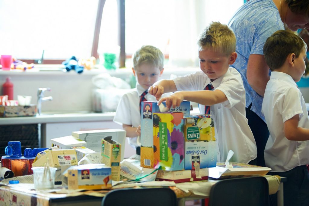 Two children putting masking tape on an old tissue box in order to build something.