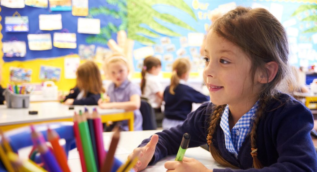 A young girl seen holding a pen and using a whiteboard to assist in her learning in the classroom.